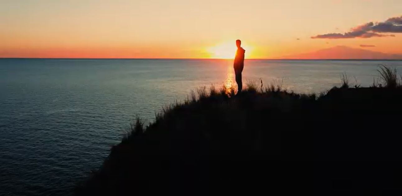Man on a cliff looking at the ocean stock footage!